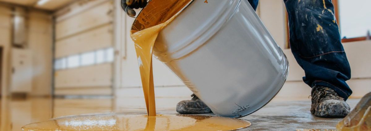person pouring yellow liquid onto a floor - Innovative Garage Flooring polyaspartic floor coating